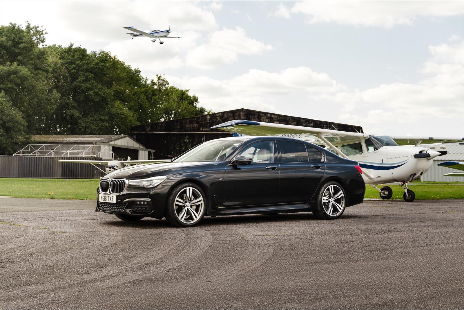 Black BMW saloon beside light aircraft at an airfield