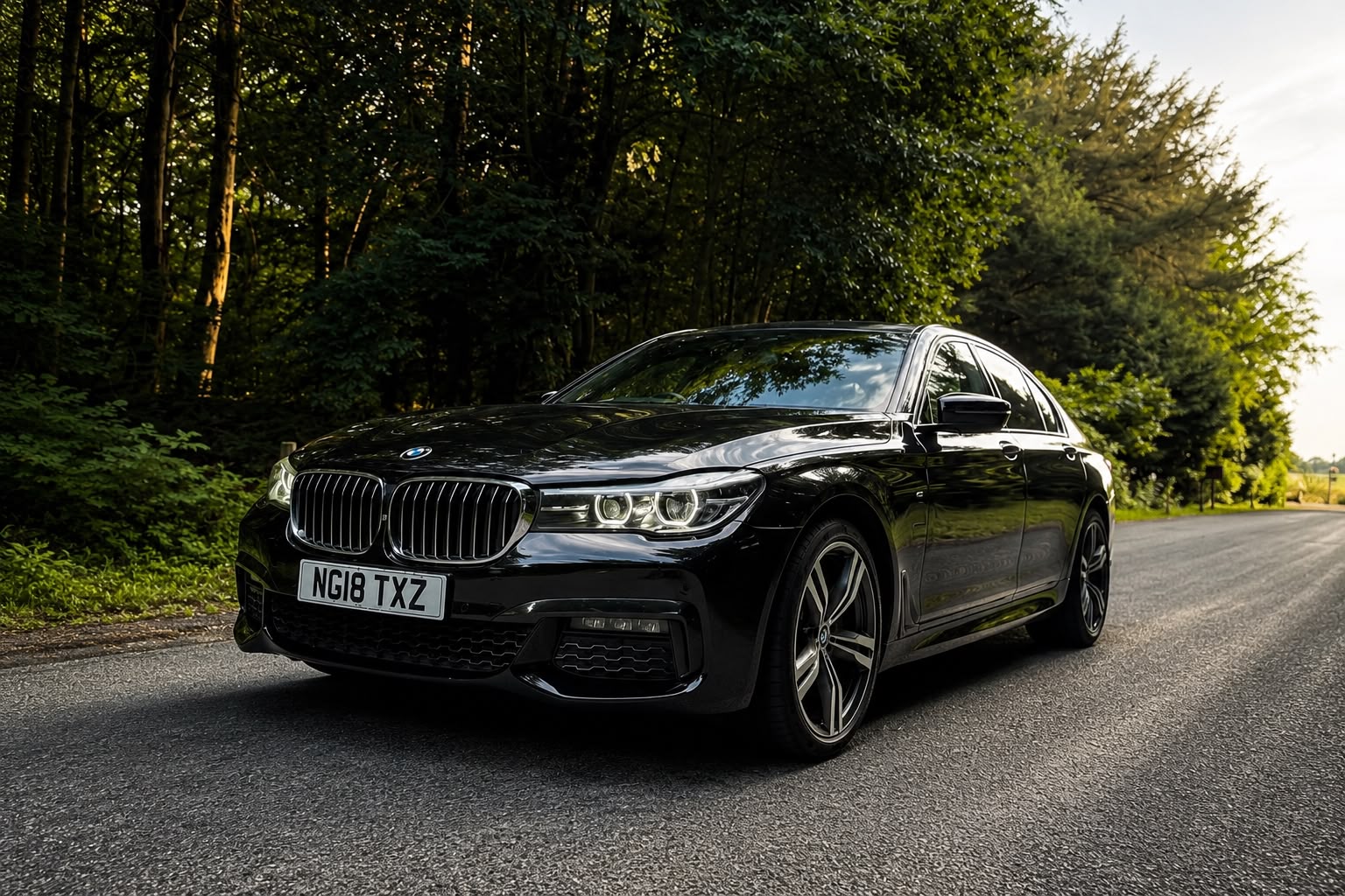 Black BMW on a quiet road beside woodland